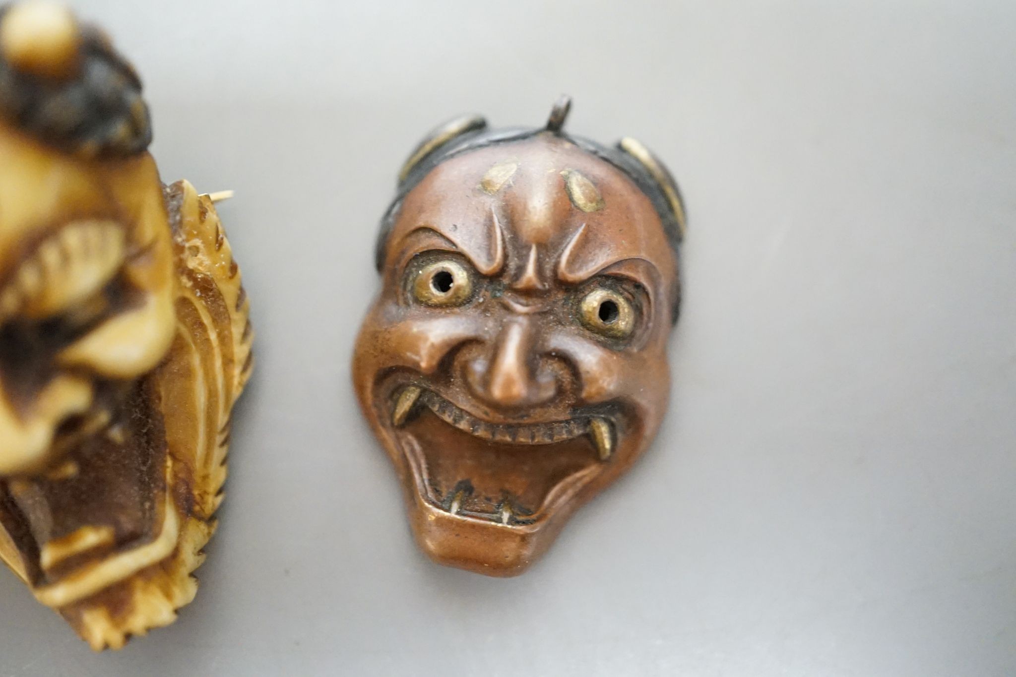 An unusual Japanese mixed metal noh mask containing minute bone dice and a stag antler noh mask brooch, signed, 3.5cm